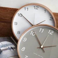 Horloge murale design Sienne de couleur taupe avec chiffres noirs, style moderne et élégant, fixée sur un mur blanc.